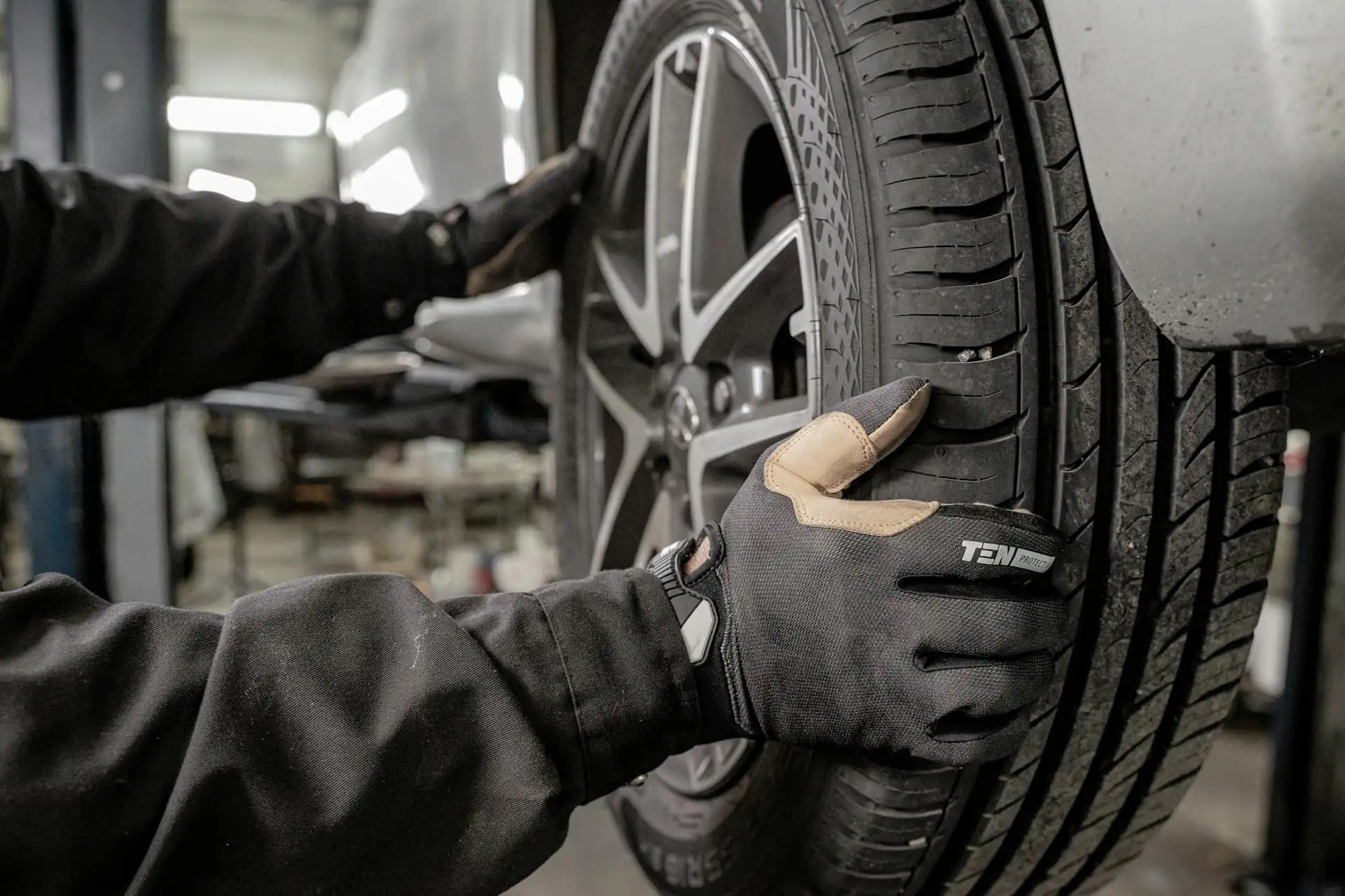 A mechanic in black gloves fitting a tyre and alloy wheel